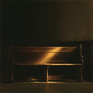 An empty wooden pew in a darkened sanctuary, crossed by a single shaft of light.